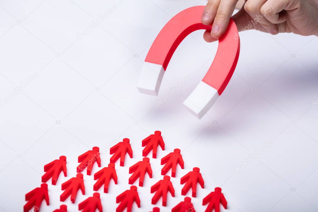 Businessman's Hand Attracting Red Team With Horseshoe Magnet On White Background