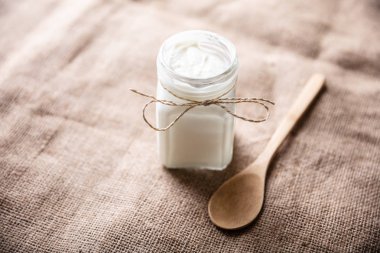 Çuval bezi üzerinde tahta kaşık yanında yoğurt ile açık bir kavanoz