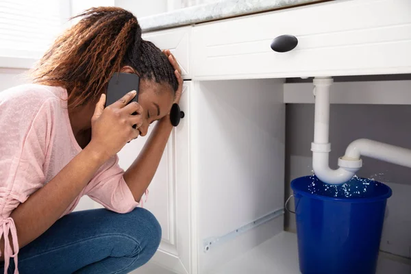 Young Woman Calling Plumber Crouching Front Water Leaking Sink Pipe — Stock Photo, Image