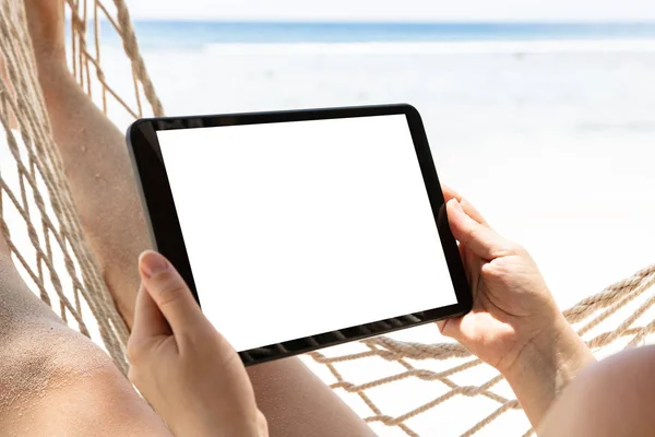 躺在吊床上的妇女的特写镜头拿着数字平板电脑 在沙滩上显示白色屏幕 — 图库照片