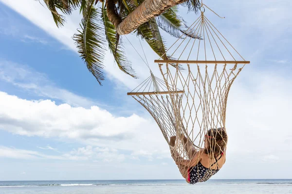 女孩放松吊床挂在棕榈树附近的海对蓝天 — 图库照片