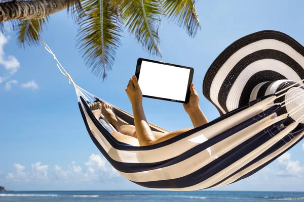 해변에서 디지털 태블릿을 사용하여 줄무늬 해먹에 모자를 쓰고있는 여성의 클로즈업 — 스톡 사진