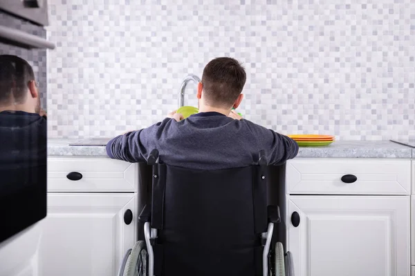 Handicapped Man Sitting On Wheelchair Washing And Cleaning Dishes In Kitchen