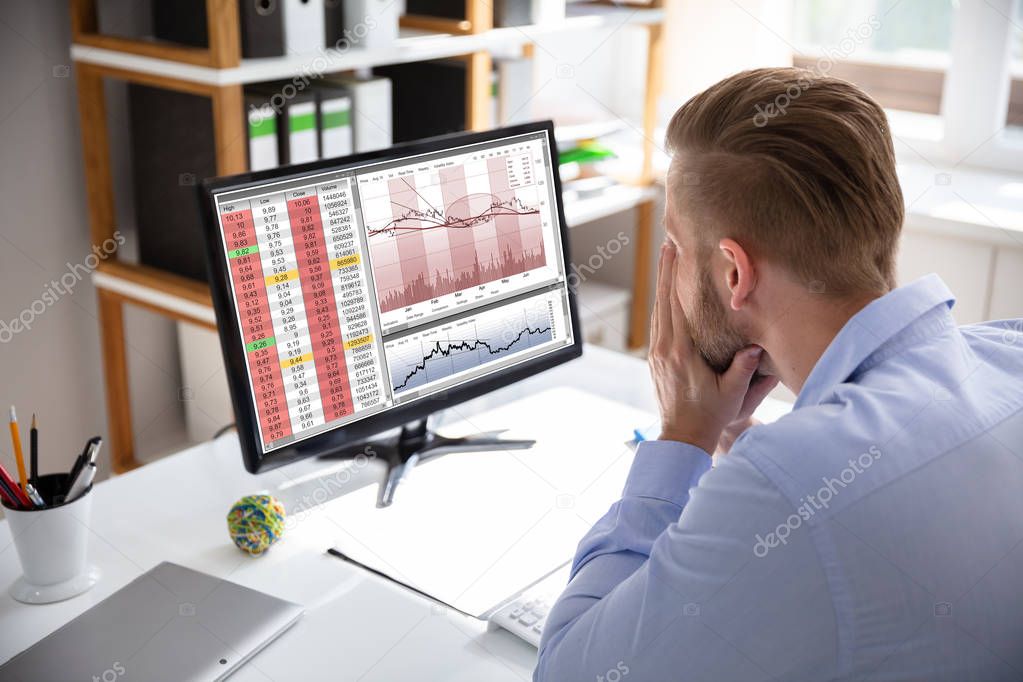 Despairing businessman faced with financial losses sitting at his desk consulting graphs on monitors