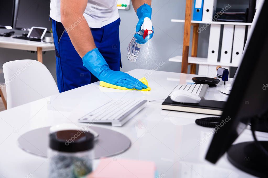 Janitor cleaning white desk in modern office