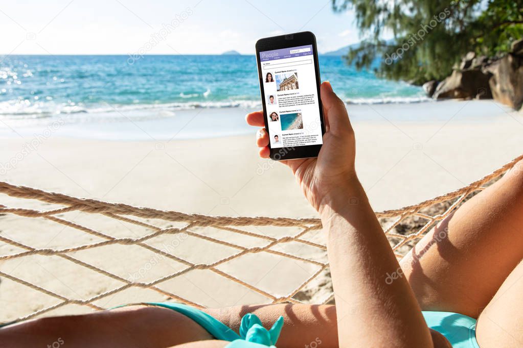Close-up Of A Woman Lying On Hammock Using Social App On Mobile Phone At Beach