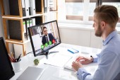 Seitenansicht von Geschäftsmann-Videokonferenzen mit Kollegen am Desktop-PC am Bürotisch