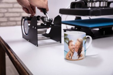 Man printing on coffee mugs in workshop clipart