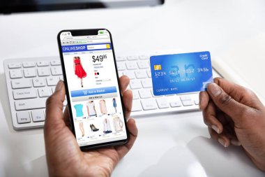 Bir kadın cep telefonu ve kredi kartı kullanarak online alışveriş yapıyor