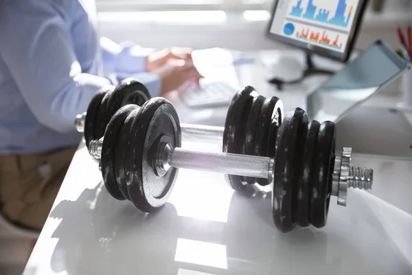 Close-up Of Dumbbells In Front Of Businessperson Working In Office