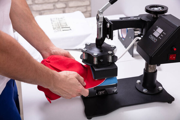 Человек печатает на бейсболке в мастерской