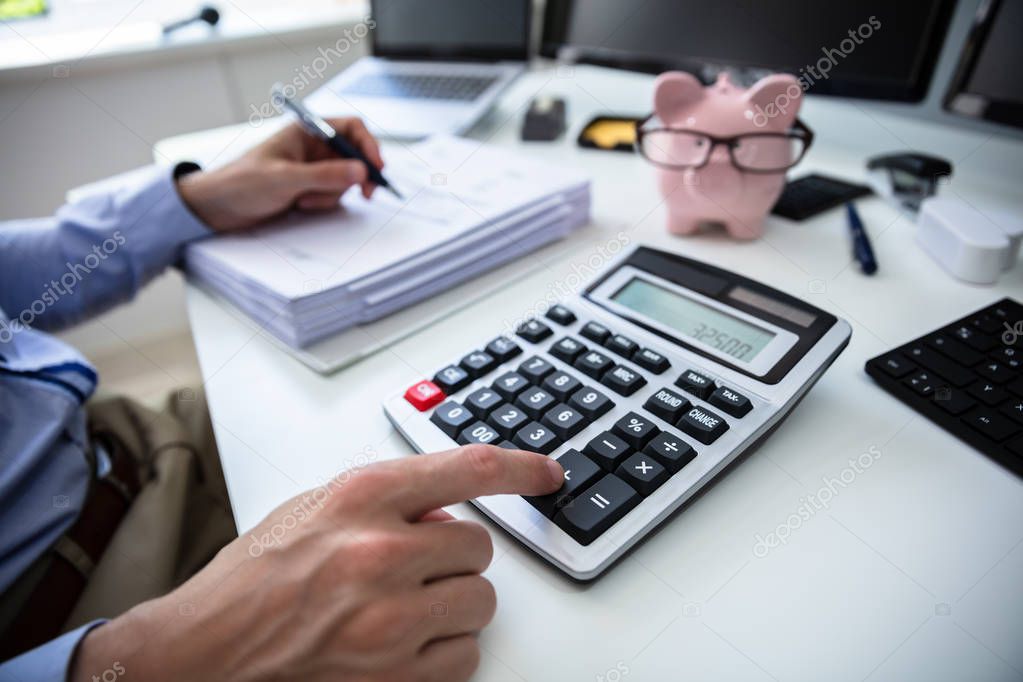 Close-up Of A Businessperson's Hand Calculating Bill With Calculator In Office