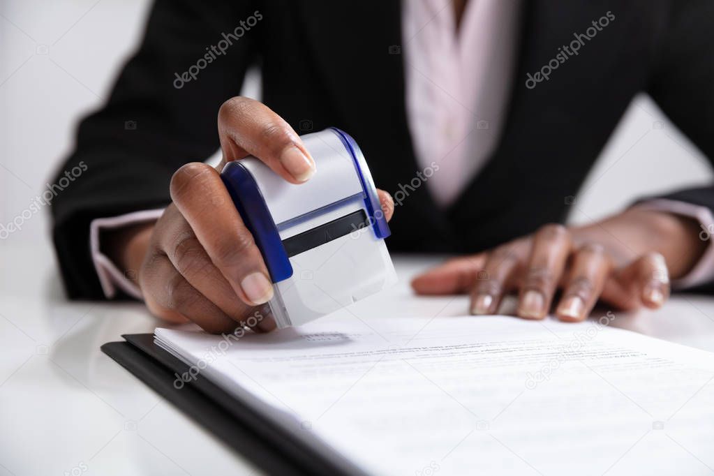 Close-up Of Businesswoman Putting Stamp On Documents In The Office