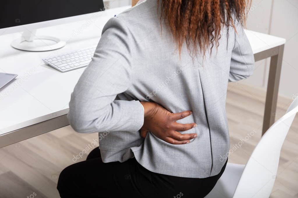 Side View Of African Businesswoman Holding Her Back While Working On Laptop At Office Desk