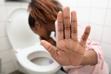 Close-up Of A Young Woman Showing Stop Sign While Vomiting In Toilet Bowl clipart