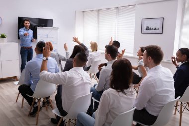 Erkek sunucu ofiste seminer sırasında el kaldırarak meslektaşına sorular soran