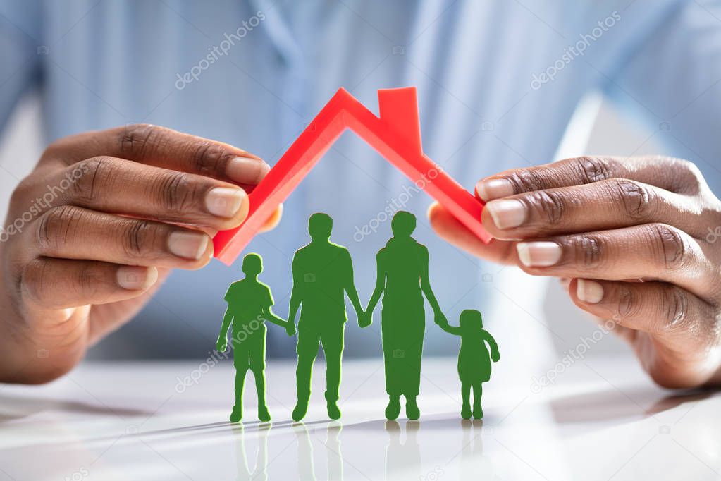 Close-up Of A Person's Hand Protecting Family Figures With Red Roof