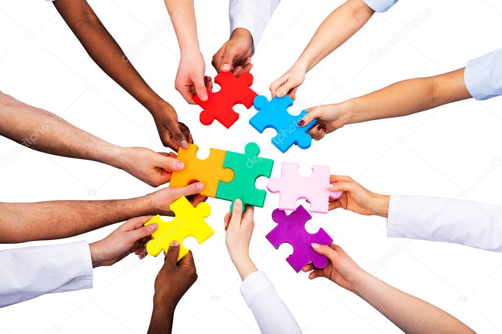 High Angle View Of Medical Team Solving Colorful Jigsaw Puzzle Against White Background