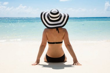 Arka görünüm Içinde bir kadın Içinde bikini oturma yakınında sahil bakıyor üzerinde deniz üzerinde plaj