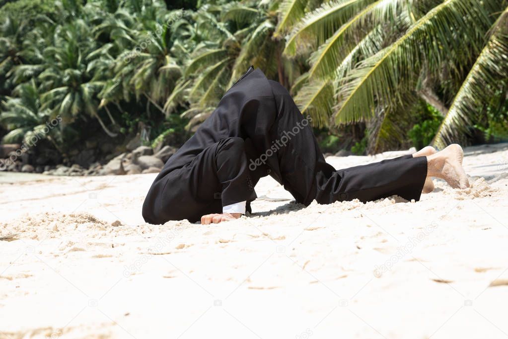 Side View Of Unsuccessful Businessman Burying His Head In The Sand At Beach
