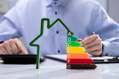 House With Energy Efficiency Rate In Front Of Businesspeople Working On Documents clipart