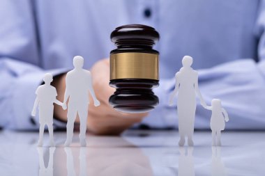 Close-up Of A Judge Striking Gavel Between Family Figure Cut Out Over Reflective Desk clipart