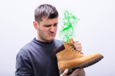 Close-up Of A Young Man Holding Stinky Shoes Against White Background clipart