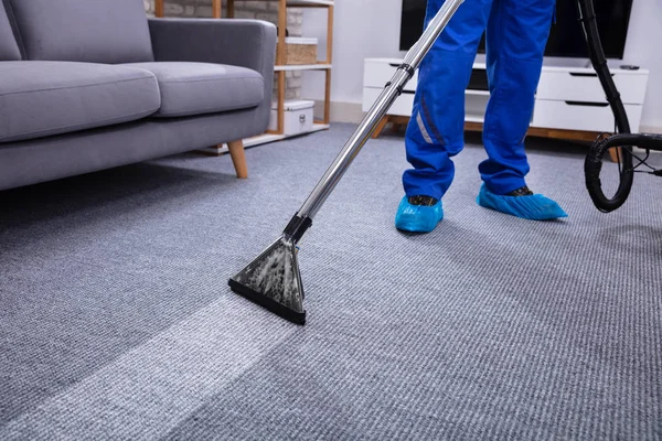 リビングルームで真空洗浄を行う男性管理人クリーニングカーペットの低部 — ストック写真