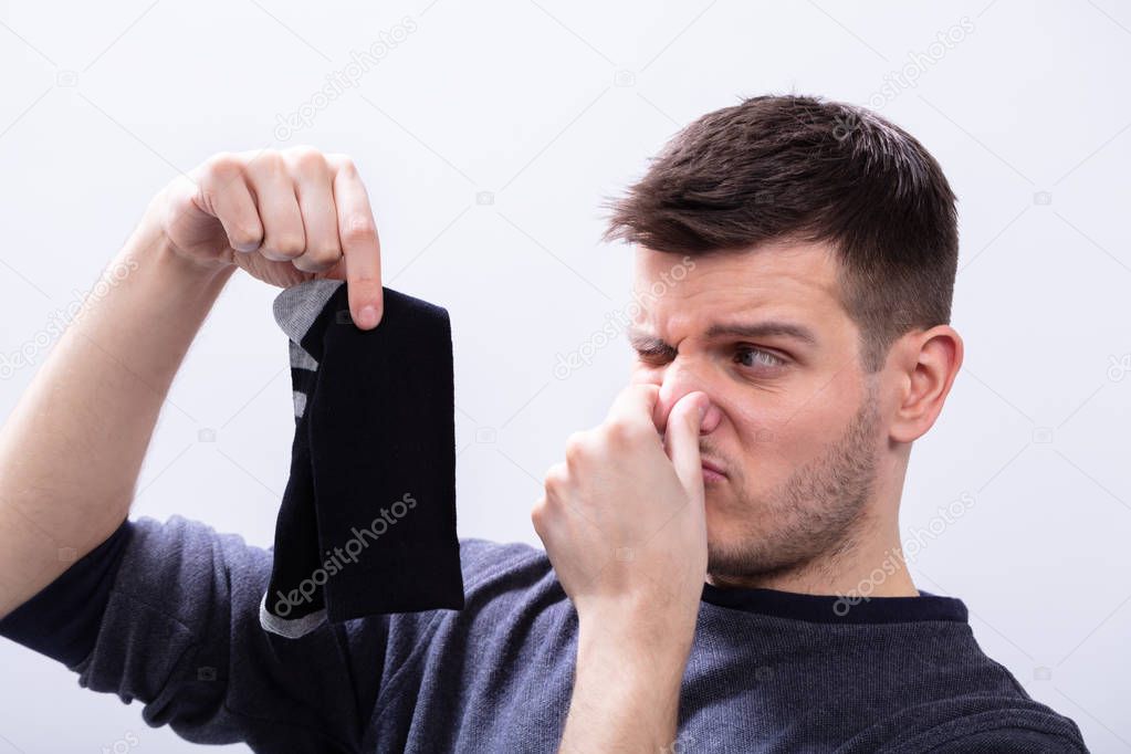 Young Man Holding His Stinking Socks Against White Background