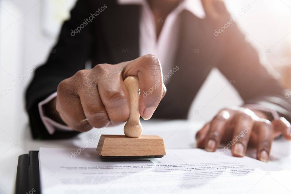 Close-up Of Businesswoman Putting Stamp On Documents In The Office