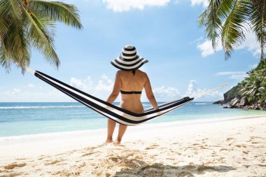 Sahilde hamak üzerinde oturan şapka Ile Bikini genç bir kadının arka görünümü
