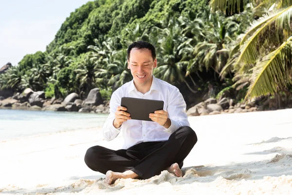 Smiling Young Man Sitting Sandy Beach His Crossed Legs Using — Stock Photo, Image