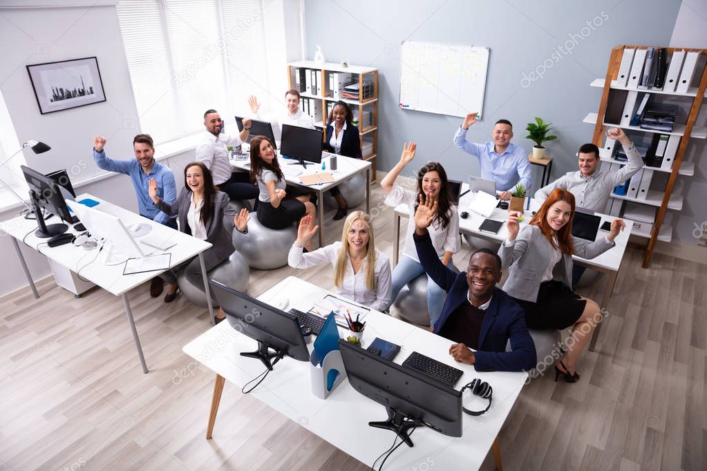 High Angle View Of Happy Multi-ethnic Businesspeople Waving Hands In Office Sitting On Fitness Ball