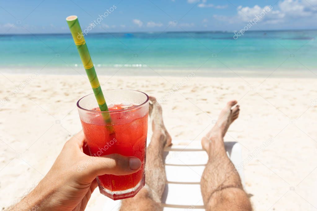 Close-up Of A Man Lying On Beach Holding Glass Of Red Juice In Hand