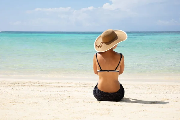 一个穿着帽子坐在沙滩上看海景的女人的后视镜 — 图库照片