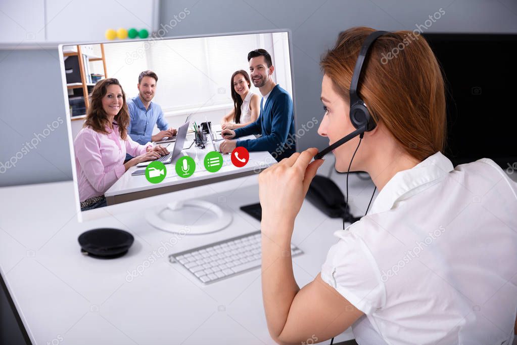 Rear View Of Businesswoman Wearing Headset While Video Conferencing With Her Colleagues