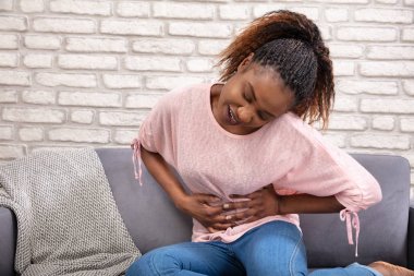 Genç kadın oturan üzerinde koltuk muzdarip gelen stomachache at ev