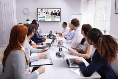 Group Of Businesspeople Having Video Conference With Another Business Team In Office clipart