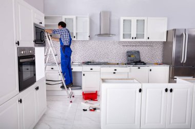 Dolabın kapısını ayarlayan merdiven üzerinde duran bir adamın arka görünüşü mutfak dolabına bağlıdır.