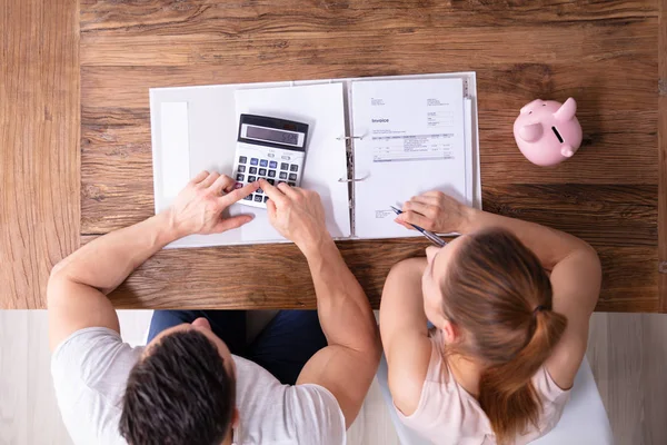 自宅で木製の机の上に電卓を使用して税金の請求書を計算するカップルのオーバーヘッドビュー — ストック写真