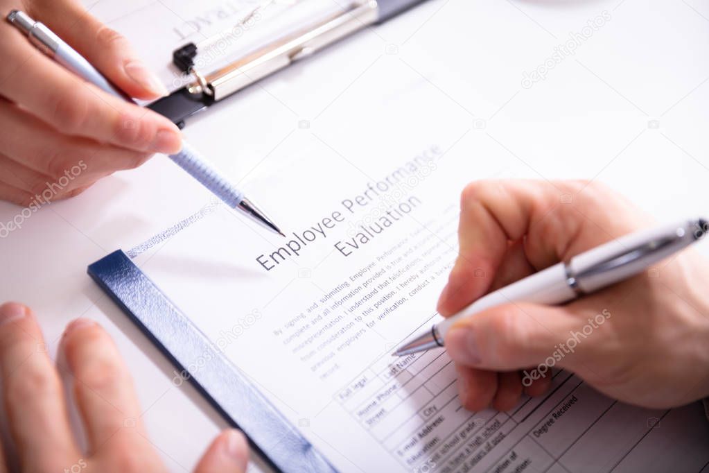 Close-up Of A Person Filling Performance Evaluation Form Of Employee Over Desk