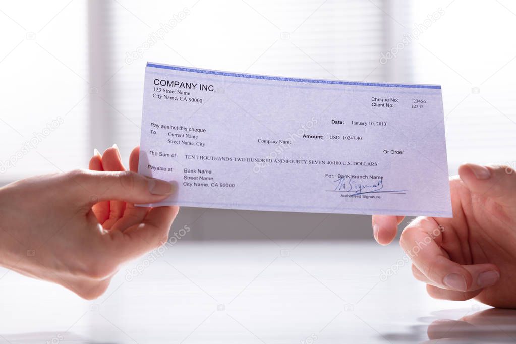 Close-up Of Woman's Hand Holding Cheque And Giving To Man