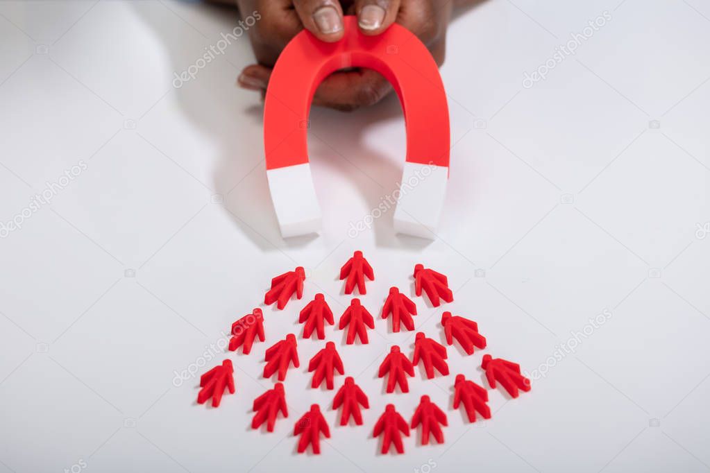 Close-up Of A Person's Hand Holding Red Horseshoe Magnet Attracting Red Human Figures