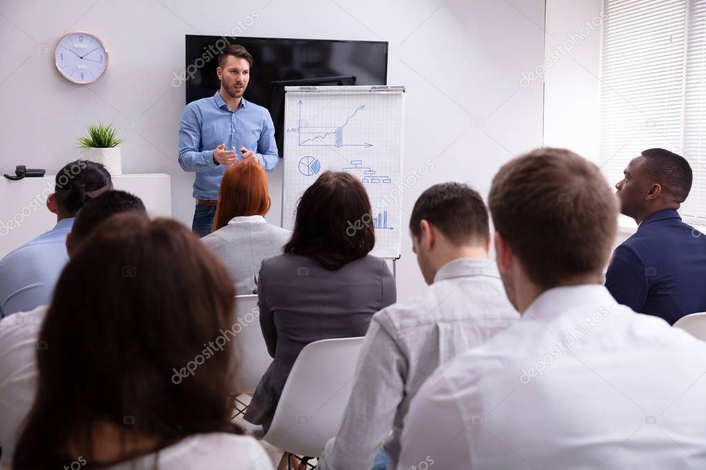 Portrait Of Handsome Young Businessman Giving Presentation To His Colleagues Sitting On Chair In Office