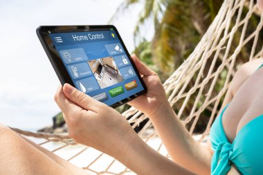 Genç kadın sahilde dijital tablet üzerinde Akıllı Ev Otomasyonu kullanarak hamak üzerinde yatıyor