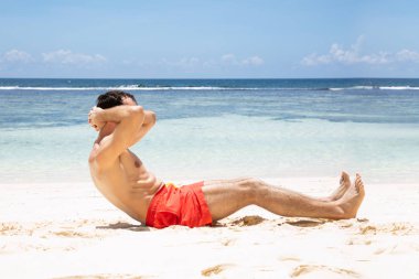 Plajda kum üzerinde Crunches yapıyor şortlu bir adam yan görünümü