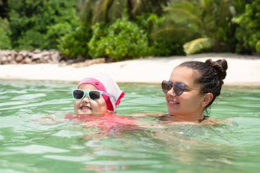 Anne ve kızının, denizde yüzen güneş gözlüğü taktığı yakın plan.