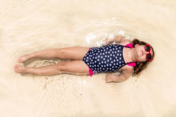 Cute Girl Wearing Sunglasses In Bikini Suit Lying On The Shallow Sea Water At Beach