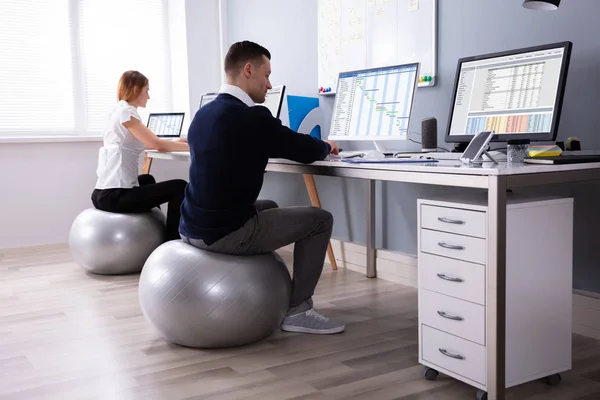Two Businesspeople Working On Computer In Office Sitting On Fitness Ball