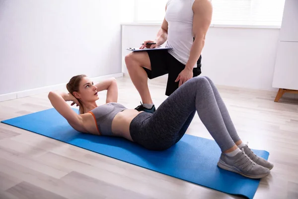 Ung Kvinna Gör Sit Ups Över Yoga Mattan Bredvid Trainer — Stockfoto